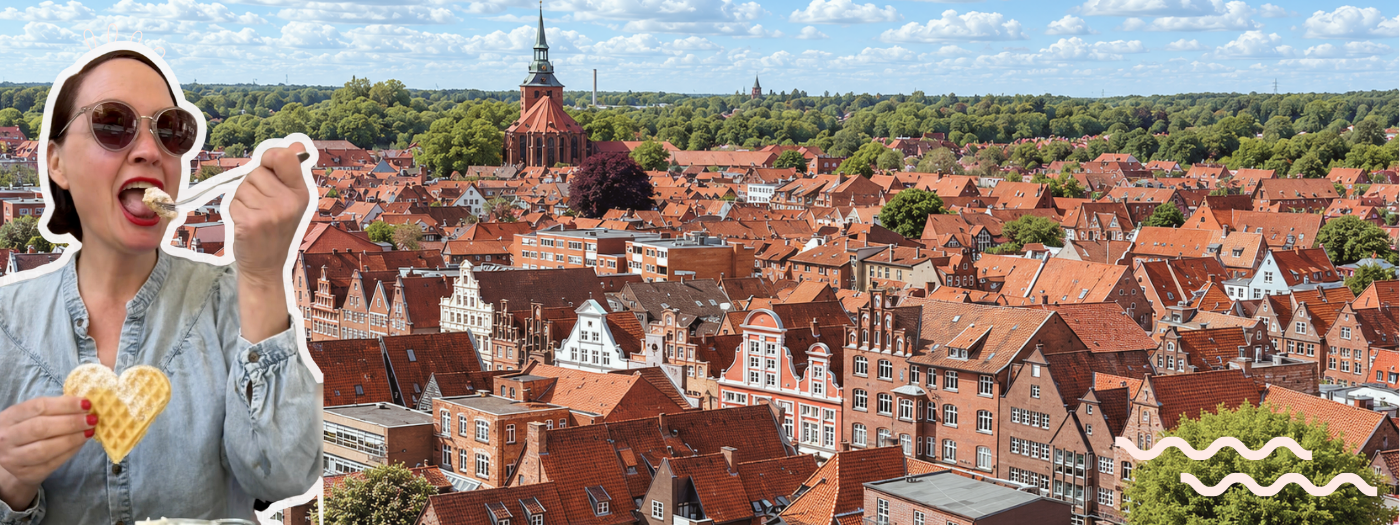 Blick über die roten Dächer der Lüneburger Altstadt mit Kirchturm, im Vordergrund Reisebloggerin Ingrid mit Sonnenbrille und herzförmiger Waffel