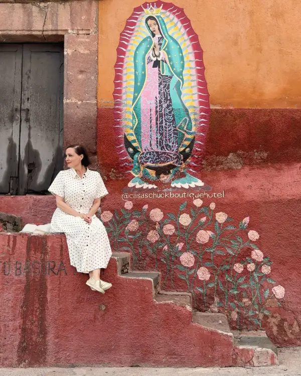 Ingrid auf einer roten Treppe unter einem Guadalupe-Wandbild in San Miguel de Allende